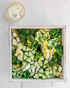 broccoli and other vegetables are arranged in a square dish with a small bowl of dip