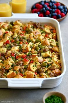 a casserole dish filled with sausage and vegetables next to oranges, blueberries, and eggs