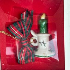 a christmas ornament in a red box with a ribbon around it and a lit candle