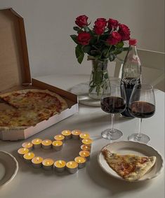 a table topped with two pizzas and glasses of wine next to a vase filled with roses