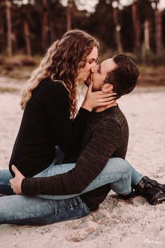 a man and woman sitting on the ground kissing each other with trees in the background