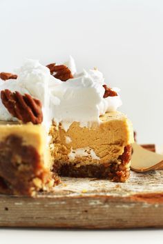 a slice of pumpkin cheesecake with whipped cream and pecans in the middle on a wooden cutting board