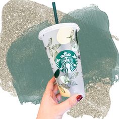 a hand holding a starbucks cup in front of a green and silver paint smudge