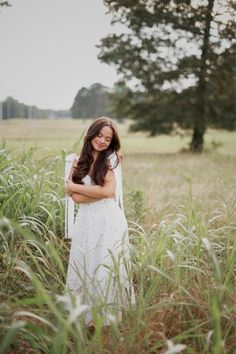 a woman standing in tall grass with her arms crossed