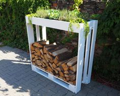 a stack of firewood sitting on top of a white bench next to a brick wall