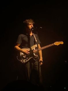 a man standing in front of a microphone while holding a guitar