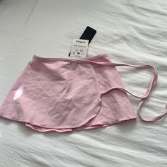 a pink skirt laying on top of a bed next to a cell phone and wallet