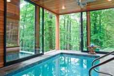 an indoor swimming pool with glass walls and trees in the backgroung area