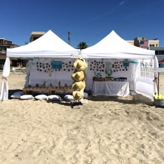 a large teddy bear sitting on top of a sandy beach next to tents and tables