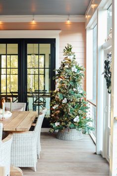 a dining room table with chairs and a christmas tree in front of the door that is open