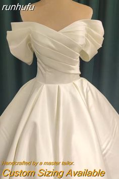 a white wedding dress on display in front of a green curtain with the words custom sizing available