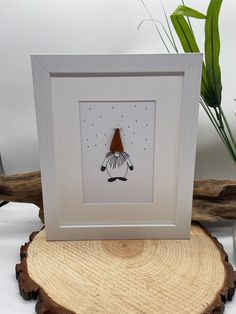 a white frame with a drawing of a bird on it sitting next to a plant