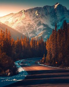 the sun shines on trees and snow in front of a mountain range with a river running through it