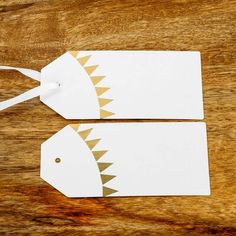 two white tags with gold designs on them sitting on a wooden table next to each other