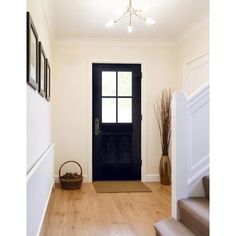 a black door is in the middle of a wooden floored entryway with stairs leading up to it