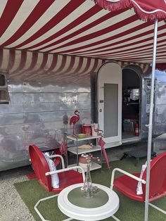 a red and white striped tent with two chairs under an umbrella next to a table