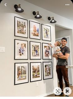 a man holding a baby in front of a wall with pictures on it