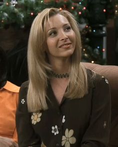 a woman sitting on top of a couch in front of a christmas tree wearing a collared shirt