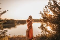 a woman in an orange dress is standing on the shore of a lake at sunset