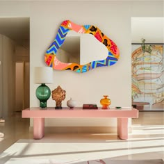 a pink table with a mirror and vases on it in front of a white wall