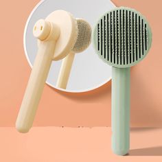 two hair brushes sitting next to each other in front of a mirror on a pink background