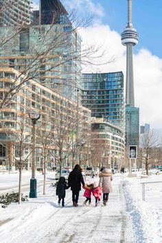 people walking in the snow on a city street with tall buildings and skyscrapers behind them