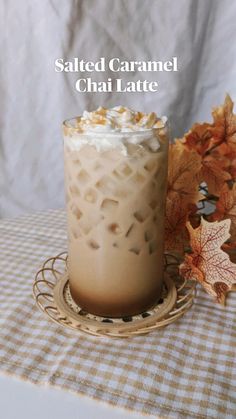 an iced drink with whipped cream in it on a plate next to leaves and a plaid tablecloth