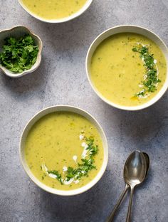 three bowls filled with soup next to two spoons