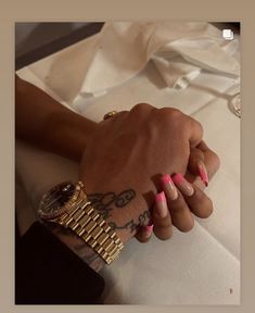 a woman's hand with pink and white manicures holding onto a watch