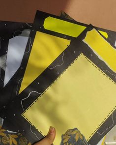 a hand is holding up some pieces of paper with yellow and black designs on it