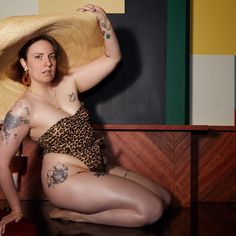 a woman in a leopard print swimsuit and hat sitting on the floor with her legs crossed