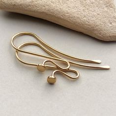 two pairs of gold earrings sitting on top of a white table next to a rock