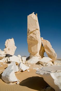 some very big rocks in the sand and blue sky with no one around them on it