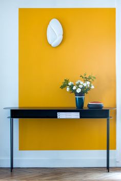 a vase with flowers sitting on top of a table in front of a yellow wall