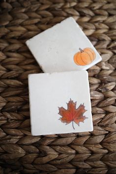 two coasters with autumn leaves on them sitting on a wicker tablecloth covered basket