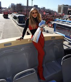 a woman in red pants and black shirt holding a silver trophy while standing on the back of a truck