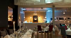 an empty restaurant with many tables and chairs set up for formal dining, in front of a bar