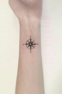 a small wrist tattoo with a compass on the left side of the arm and an arrow in the middle