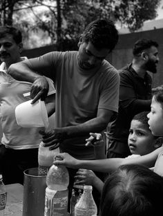 a group of people standing around a table filled with bottles and jugs on top of it