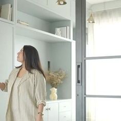 a woman standing in front of a white bookcase with open doors and shelving unit behind her