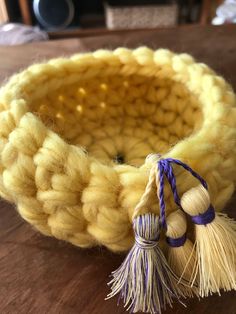 a crocheted basket sitting on top of a wooden table with two tassels hanging from it