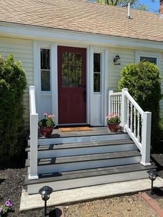 a red door sits on the front steps of a white house with potted plants