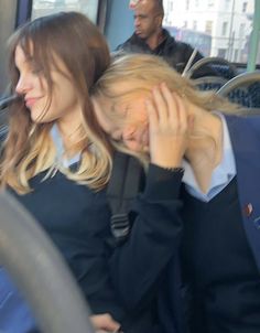 two women are sitting on a bus and one is holding her head