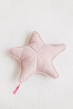 a pink star shaped pillow with a tassel hanging from it's side on a white surface