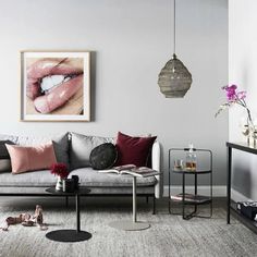 a living room with grey couches and pink pillows on the floor next to a coffee table