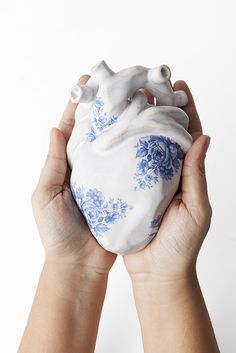 two hands holding a white and blue heart shaped object in it's left hand