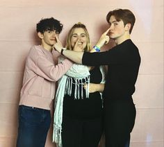 three people standing next to each other in front of a pink wall