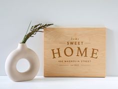 a white vase sitting next to a wooden sign that says sweet home with a plant in it