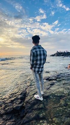 a man standing on top of a rock covered beach next to the ocean under a cloudy blue sky