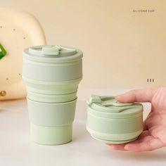 a hand holding a cup next to a green coffee cup on a white countertop